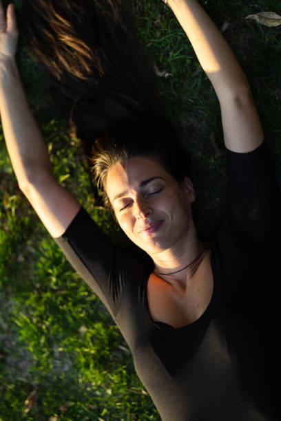 Happy mid adult woman lying on back and relaxing in grassy field on sunny day