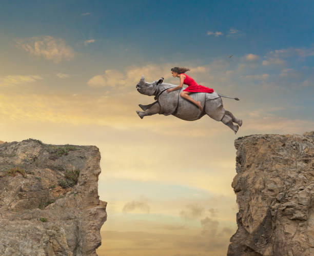Young woman riding a rhinoceros across a gap between cliffs