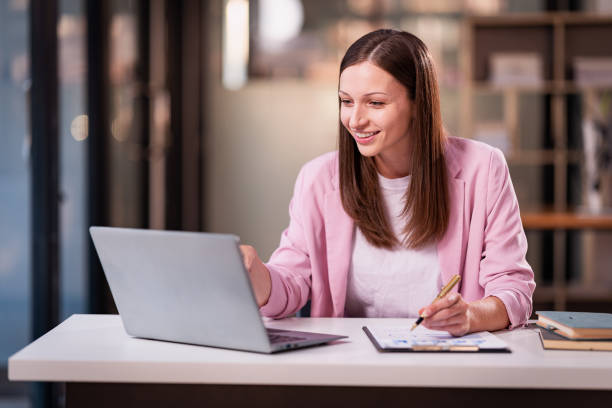 istock Beautiful professional woman sitting at table smiling while reading important documents with financial graphs and accounting of company. 2179509521