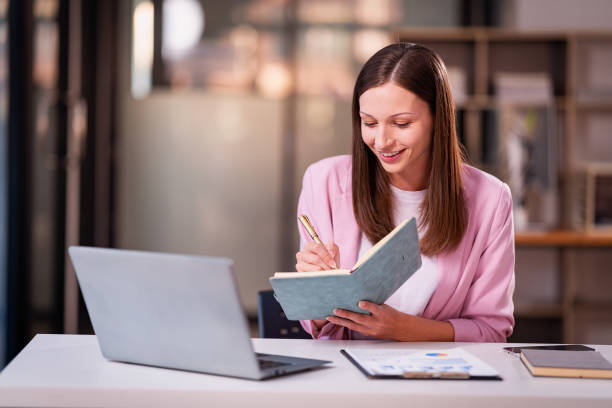 istock Beautiful professional woman sitting at table smiling while reading important documents with financial graphs and accounting of company. 2179509523