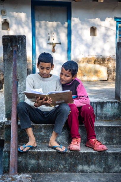 Two young boys share a book while seated on stone steps, absorbed in their reading. The bright surroundings enhance their joyful learning experience. concept of education, technology and knowledge