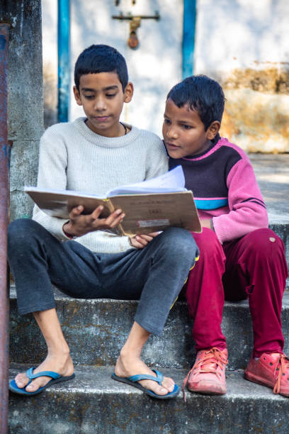 istock Two boys sitting on stone steps reading a book together outdoors in a sunny environment 2179510101