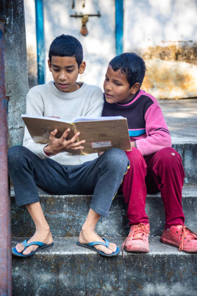 Two young boys share a book while seated on stone steps, absorbed in their reading. The bright surroundings enhance their joyful learning experience. concept of education, technology and knowledge