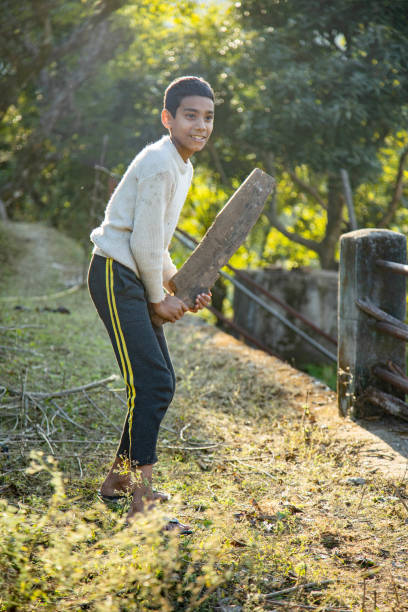 Poor Indian village boys playing cricket  with hand made ball on a green field on top of a hill in the Himalayan village.