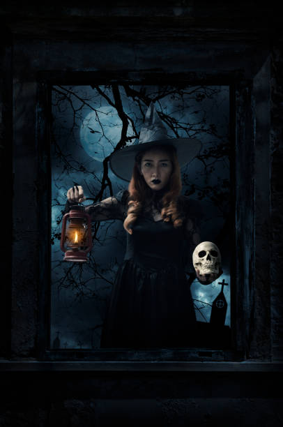 Halloween witch holding ancient lamp and skull standing in old damaged wood window with wall over cross, church, birds, dead tree and spooky cloudy sky, Halloween mystery concept