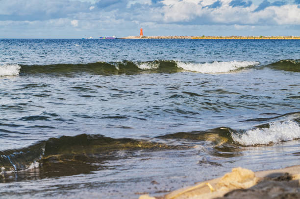 Waves lapping on the sandy shore, Baltic sea seascape. Red lighthouse on the horizon and dramatic sky