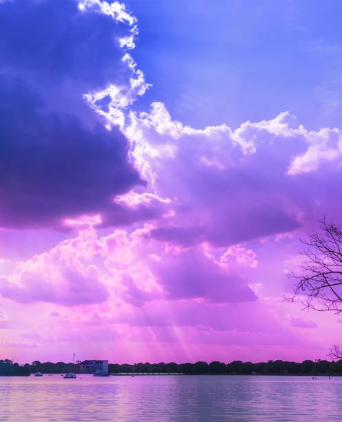 Vibrant purple and blue sunset over a serene lake with dramatic clouds and sun rays, capturing a tranquil evening scene.