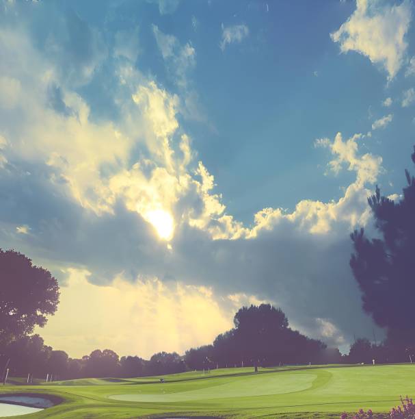 Scenic view of a golf course with sunbeams breaking through clouds in a vibrant sky, surrounded by lush greenery.
