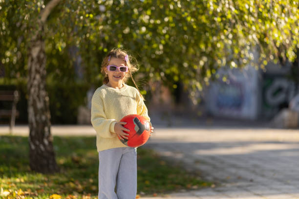 Portrait of cute girl in yellow sweater standing and holding ball in autumn park