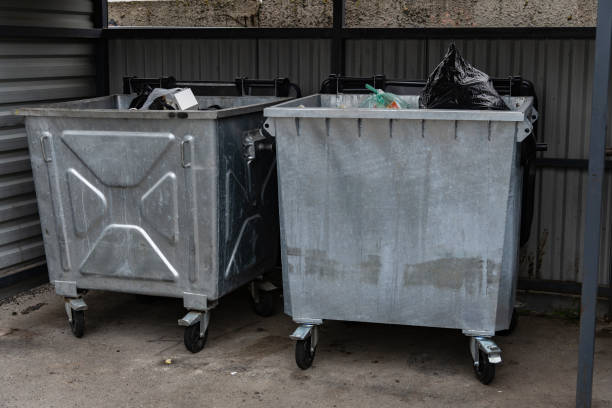 istock In an urban setting, two large metallic garbage containers are parked on wheels. One is filled with black trash bags, while the other contains various recyclable items 2179532267