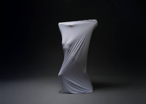 A mysterious figure wrapped in white fabric poses against a dark backdrop, creating an intriguing visual contrast and evoking emotion.