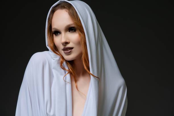 istock Elegant model in white draped fabric poses gracefully against dark backdrop 2179544529