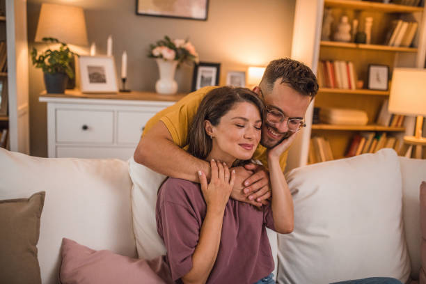 istock A smiling man hugs his smiling girlfriend who is resting on the sofa 2179545783