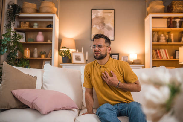 istock Depressed man has severe chest pain while sitting on sofa in living room 2179549304