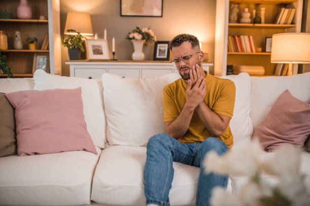 istock Man has severe toothache while sitting on sofa in living room 2179549543