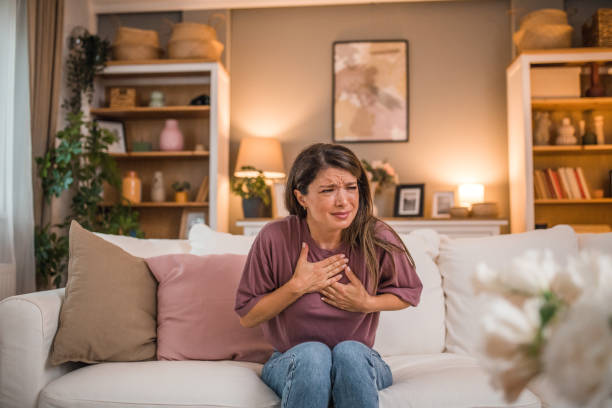 istock Woman has severe chest pain while sitting on sofa in living room, possible heart attack 2179549708
