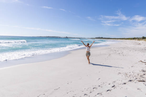 A solitary woman strolls along a pristine, white sandy beach with turquoise waters and clear blue skies on a sunny day.