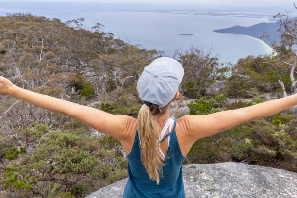 A woman with outstretched arms stands on a mountain top, embracing the scenic view of the coastline and ocean below, symbolizing freedom and joy.