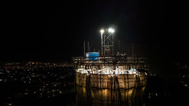 Illuminated construction site at dusk.Dangerous work at the nighttime.Workers build a tall chimney for a plant.Construction process.Contractor renovation is smokestack on highrise.Worker in hardhat