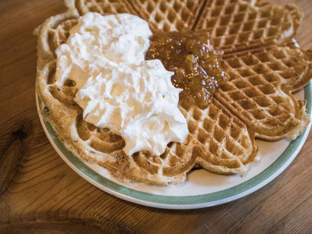 Table set with sweet dessert waffle dish with whipped cream and cloudberry jam.