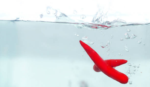 A vibrant red pepper dropped into clear water, creating gentle ripples and bubbles as it descends, contrasting beautifully with the transparent water