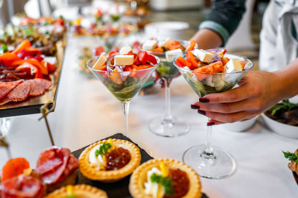 istock A close-up of a buffet table with an array of gourmet appetizers, including martini glasses filled with fresh salad and tartlets topped with cream and fruit, in a party setting. 2179594342
