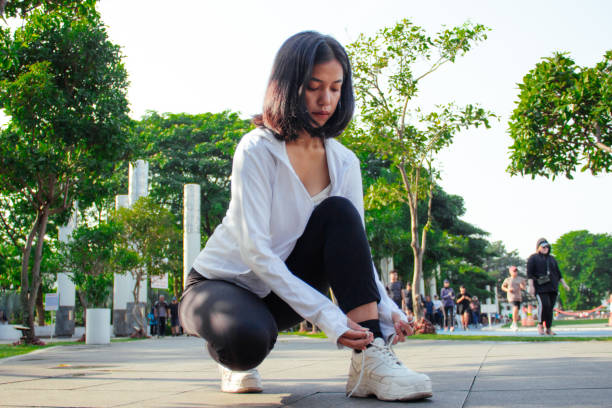 A woman tightens her shoelaces, preparing for her morning run with focus and determination. Wearing sustainable sports gear, she demonstrates a mindful approach to fitness, balancing performance and environmental awareness.