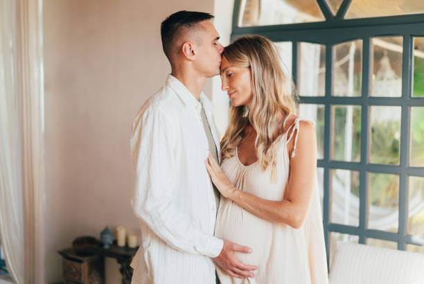 istock A pregnant couple stands hugging inside. 2179602749