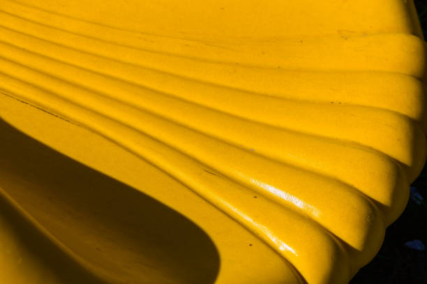 The inviting yellow bench, bathed in sunlight, features elegant curved lines that enhance its playful design, making it a perfect spot for leisurely moments in the park.