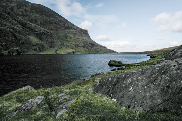 Dramatic cloudy sky frames a serene mountain lake surrounded by lush, verdant slopes in a remote, picturesque natural setting.