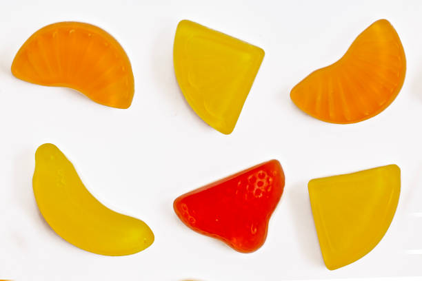 A macro close-up of a variety of fresh cut fruits on a black plate. Visible fruits include slices of banana (Musa), apple (Malus domestica), segments of orange or mandarin (Citrus spp.), and red grapes (Vitis vinifera). The fruit pieces are arranged without a specific pattern, showcasing their vivid colors and textures against the dark background. The soft lighting highlights the freshness and juiciness of the fruits, enhancing their natural appeal.