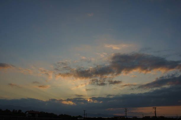 As day transitions to night, vibrant clouds dance in the sky, blending shades of orange and blue. Power lines silhouette against this peaceful backdrop, evoking tranquility.