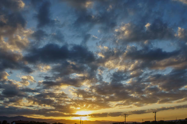 The sun dips below the horizon, casting a warm glow across the sky, where fluffy clouds gather in a stunning array of colors, creating a serene evening atmosphere.