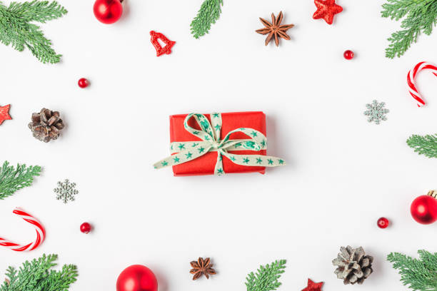 istock Christmas present in frame made of fir branches, red decorations, candy and pine cones on white background. Flat lay. Happy New Year and winter holidays background. Top view 2179642395