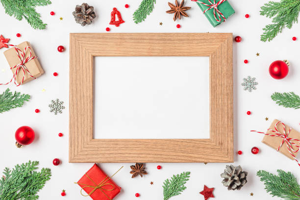 istock Blank photo frame with Christmas decorations, fir branches, gift boxes, pine cones on white background. Flat lay. Mock up. Happy New Year and winter holidays background. Top view 2179642578