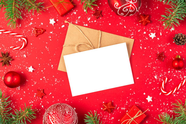 istock Christmas greeting card and envelope in frame made of fir branches, gift boxes, decorations, candy and pine cones on red background. Flat lay. Mock up. Happy New Year and winter holidays invitation 2179642723
