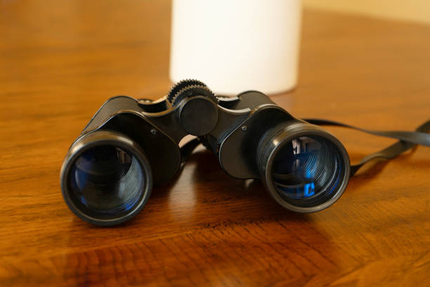 Low angle close up of black binoculars laying on a wood table.