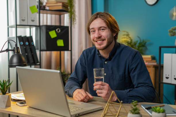 istock Business man sitting at workplace desk drinking water while working with laptop in home office 2179654130