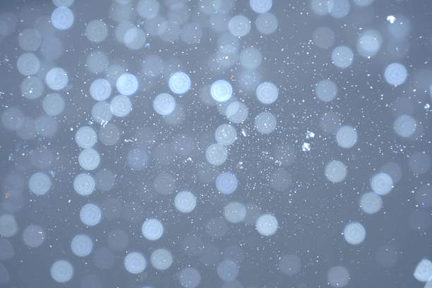 Snowfall with a bokeh effect, where snowflakes create a tranquil symphony of blurred light dots against a cool, grey background.