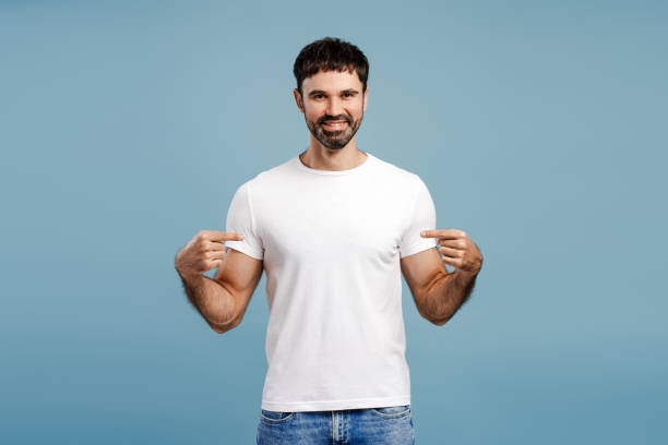 istock Smiling, bearded man wearing white t shirt, pointing finger, mockup, copy space, looking at camera 2179675954