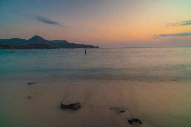a mossy rock on the beach exposed to the waves at sunset