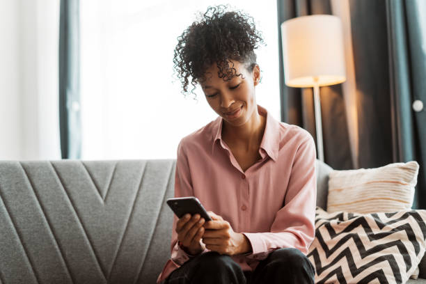 istock Young woman is relaxing at home on a comfortable sofa, smiling while using smartphone 2179679699