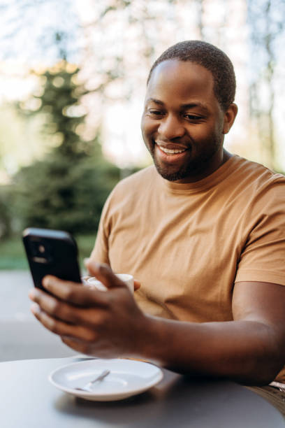 istock Happy African American man drinking coffee using smartphone at cafe outdoors 2179680803