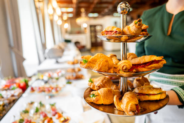 istock A three-tiered serving tray with assorted pastries, held by a person in a green top, with a blurred buffet background. Perfect for high tea, catering, or dessert presentations. 2179706753