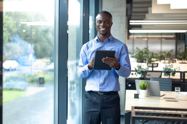 istock Smiling busy african businessman manager using tablet computer, executive looking at camera standing in office 2179707092