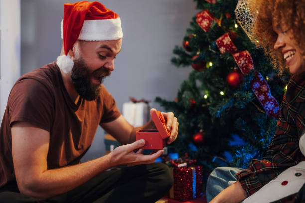 istock Bearded man opening christmas gift with girlfriend near christmas tree 2179733789