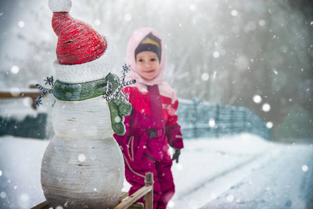 Children build snowman. Kids building snow man playing outdoors on sunny snowy winter day. Outdoor family fun on Christmas vacation. Boy and girl play snow balls. Winter clothing for baby and toddler.