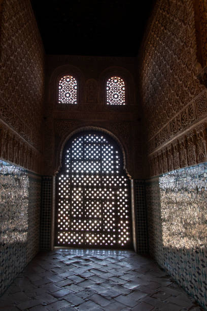 Granada, Spain-February 7, 2024; Light shining through lattice panel in window on marble floor and tiled and decorated walls of The Alhambra palace, with Islamic and Spanish architecture