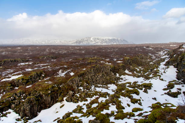 Panoramic view of Hrafnagja canyon or seismic rift valley between Eurasian and North American tectonic plates in Thingvellir National Park, Iceland with snow topped mountains in background