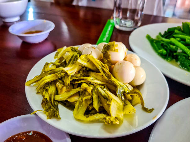 A high-quality image featuring rau cải & cà pháo muối chua, a classic Vietnamese fermented dish. It combines tangy pickled mustard greens with crunchy fermented white eggplants (cà pháo). This dish offers a perfect balance of sour, salty, and slightly spicy flavors, often enjoyed as a refreshing side dish with braised meats, rice, or soups. The vibrant colors and distinct textures make it both appetizing and essential in Vietnamese home cooking. Ideal for food photography, restaurant menus, or content focused on traditional Vietnamese pickling techniques and rustic meals.